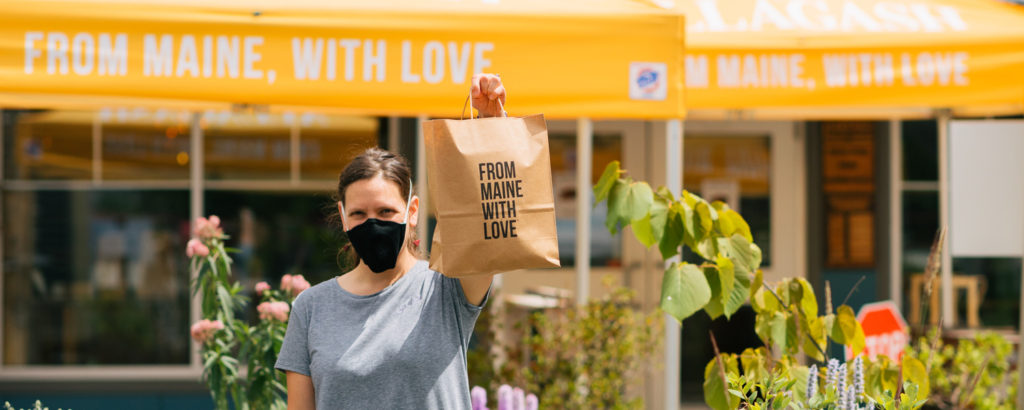 Woman holding up bag saying 'from Maine with love' while wearing mask, Photo Courtesy of Mat Trogner, via Allagash Brewing Woman holding up bag saying 'from Maine with love' while wearing mask, Photo Courtesy of Allagash Brewing and their staff